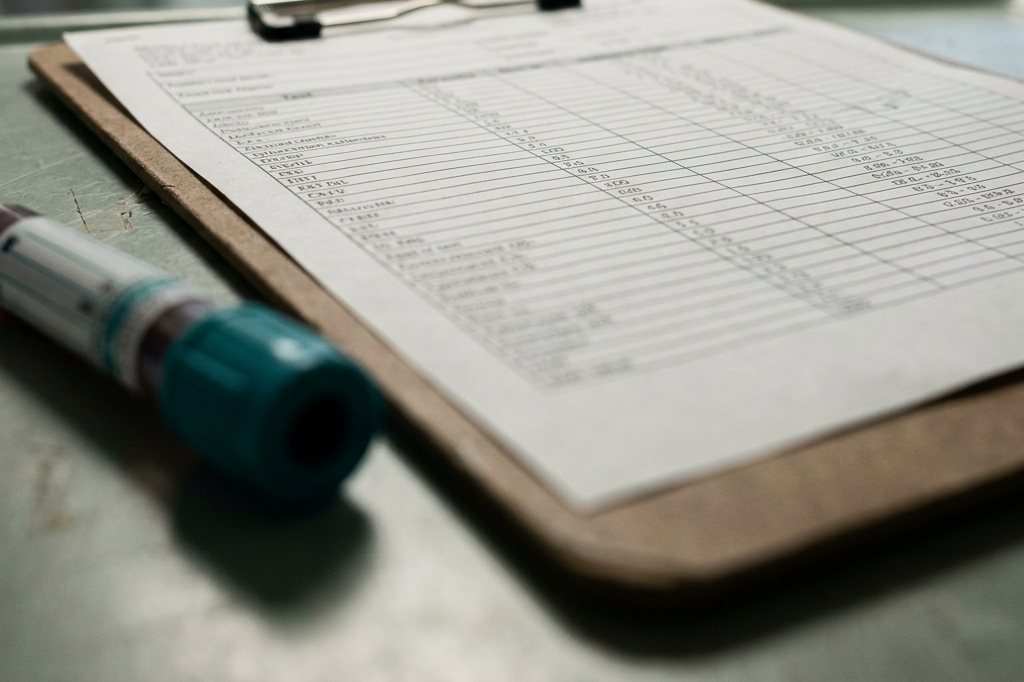 A laboratory panel printout on a clipboard beside a blood collection tube.